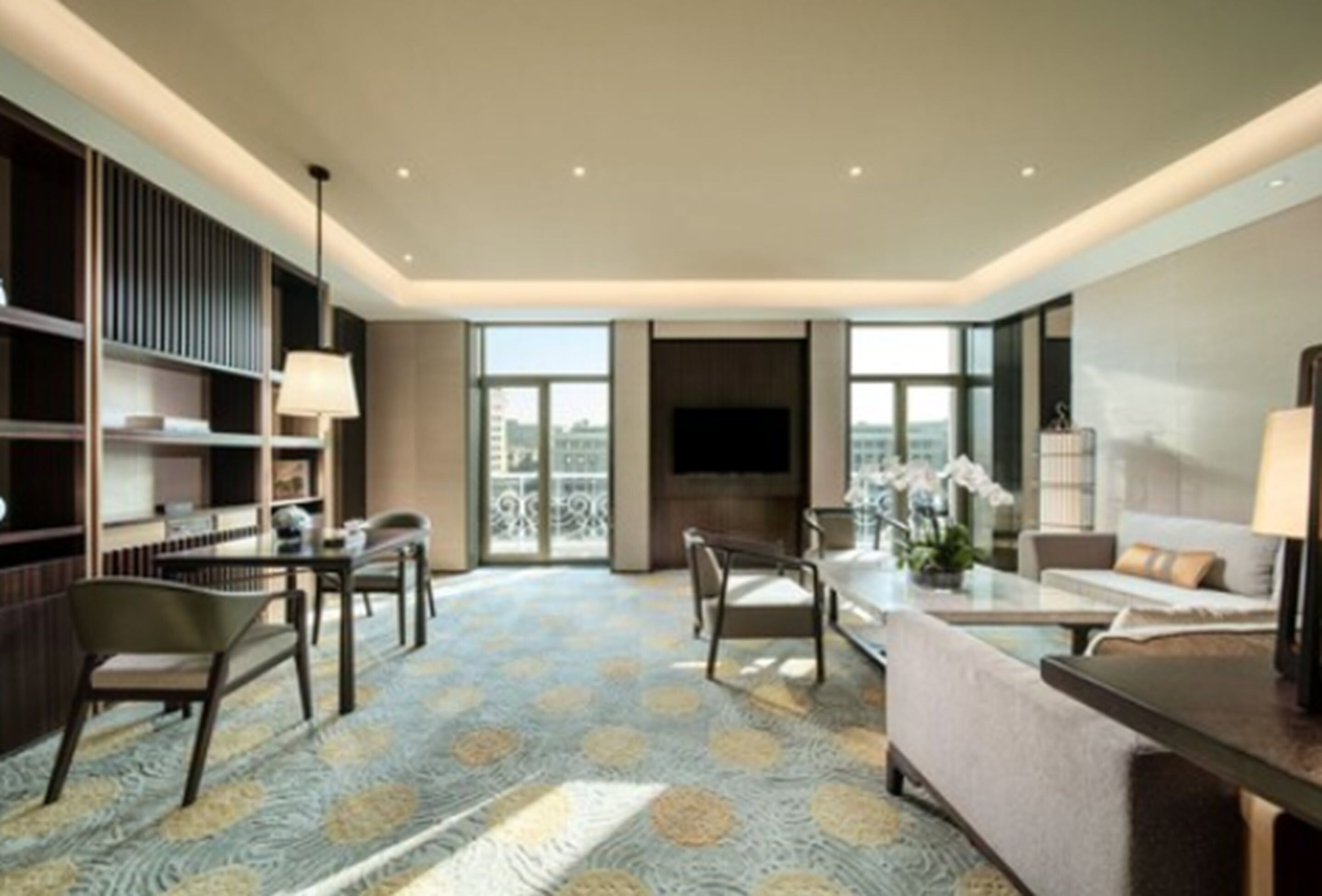 A modern hotel room with a large window, a flat-screen TV, a sofa, a coffee table, and a bookshelf.