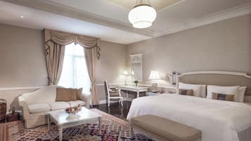 A hotel room with a large bed, a sofa, a desk, and a patterned rug.