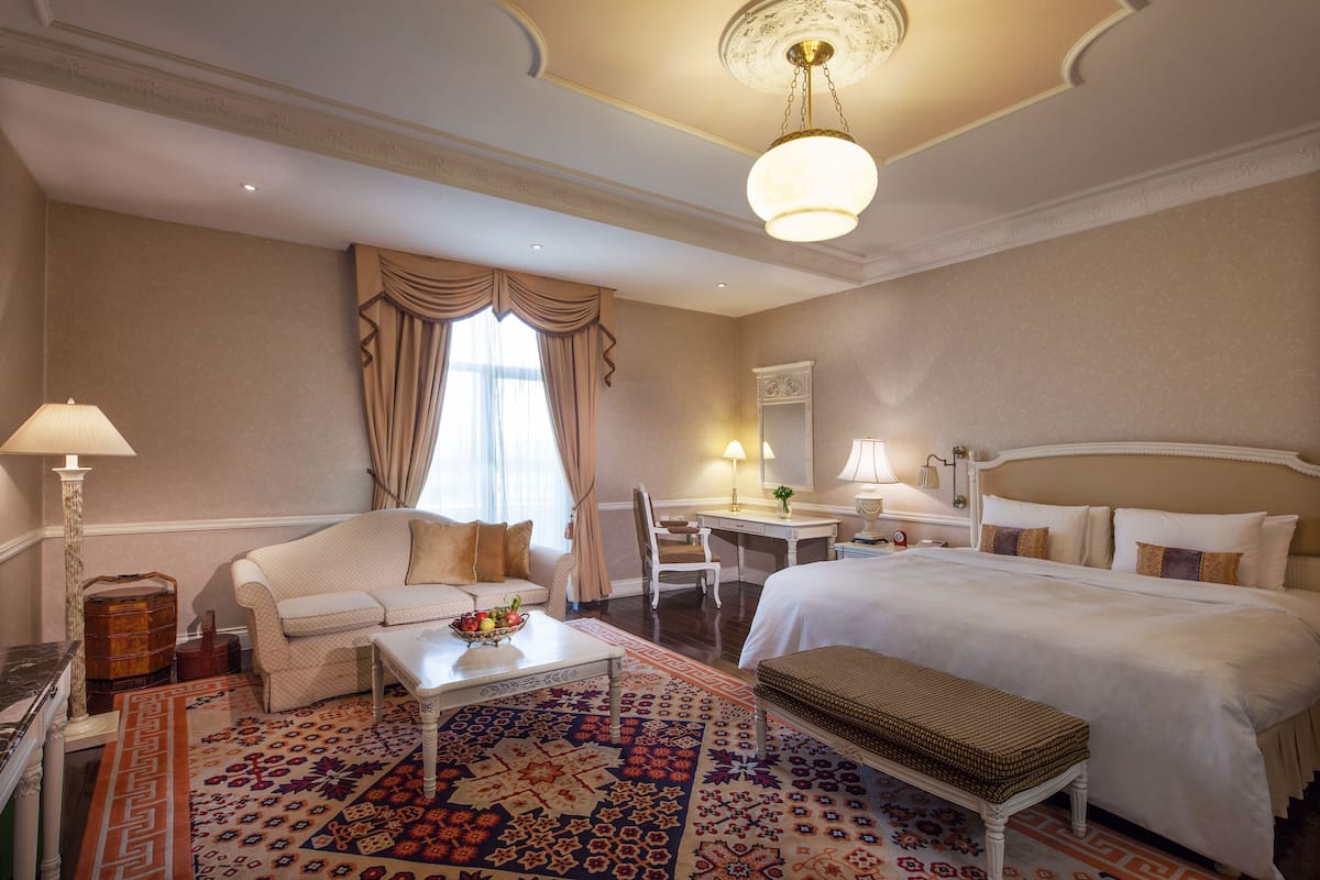 A hotel room with a large bed, a sofa, a desk, and a dining table.