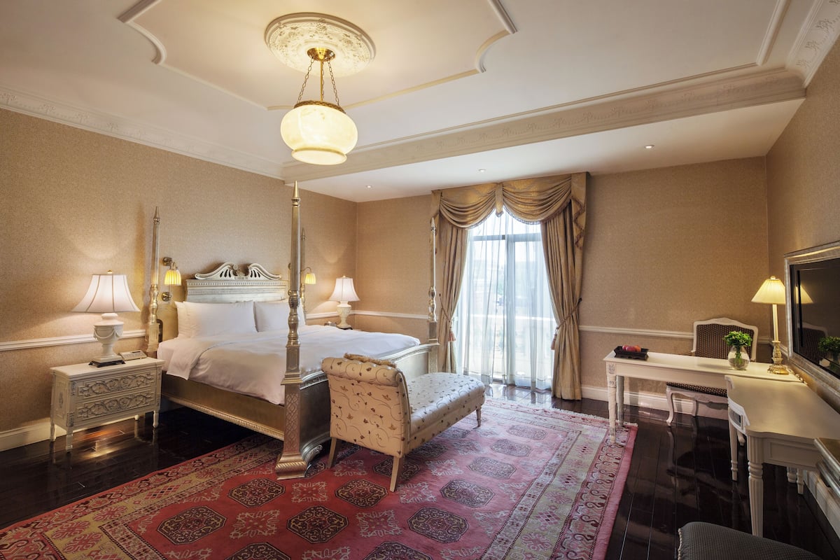 A hotel room with a large bed, a sitting area, a desk, and a chandelier.