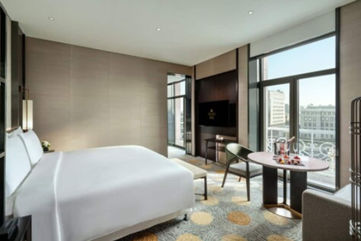 A modern hotel room with a large bed, a small table, a chair, and a TV.