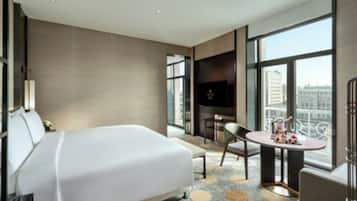 A modern hotel room with a large bed, a small table, a chair, and a TV.
