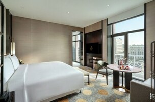 A modern hotel room with a large bed, a small table, a chair, and a TV.