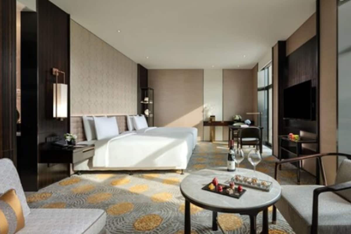 A modern hotel room with a large bed, a desk, a TV, and a dining area.