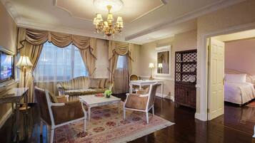 A spacious hotel room with a large bed, a sitting area with a sofa and armchairs, a dining table, and a chandelier.