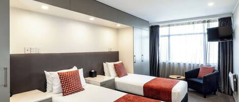 A hotel room with two beds, a TV, a chair, and a window with curtains.