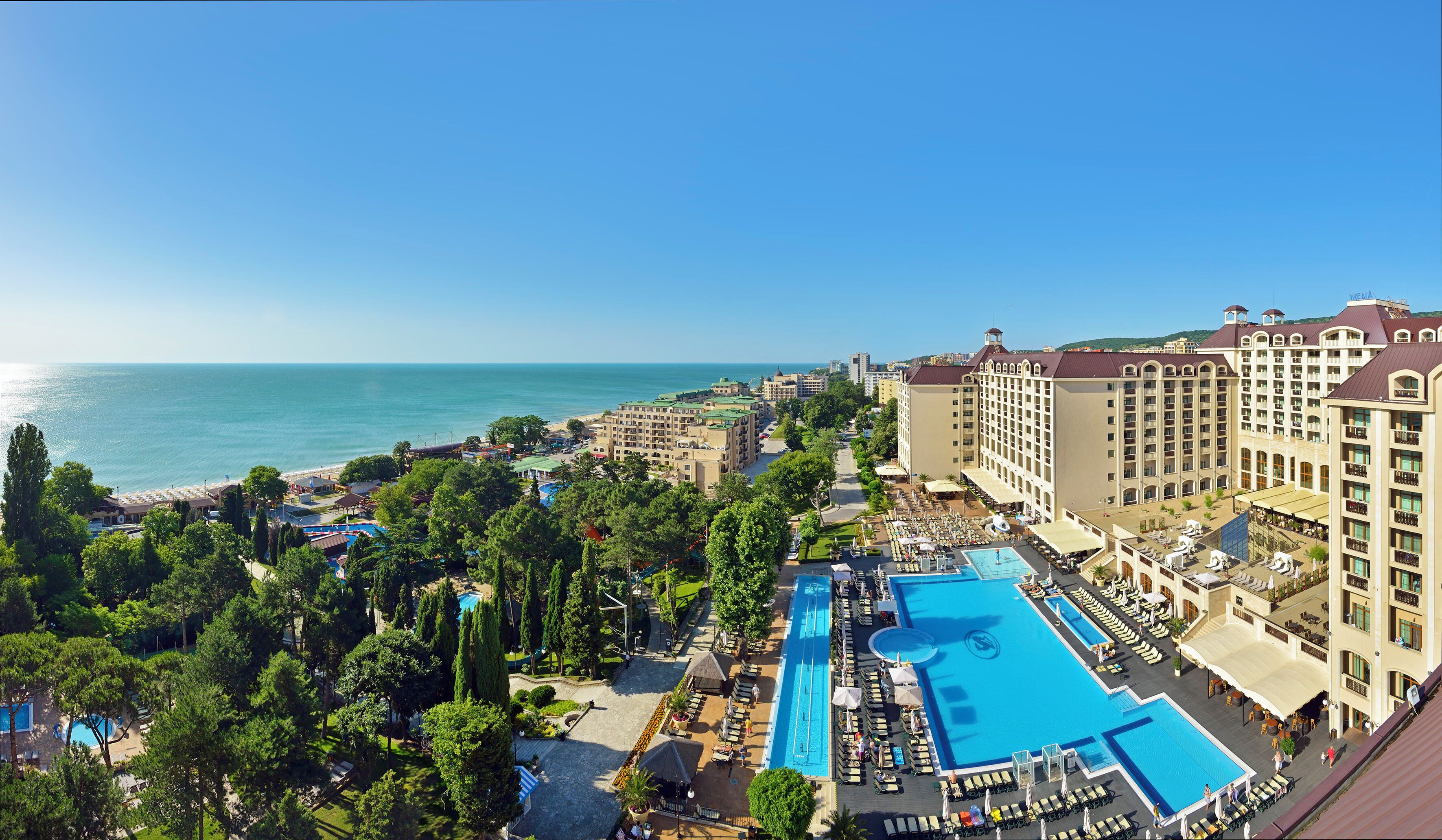 A resort with a large pool, multiple buildings, and a beach view.