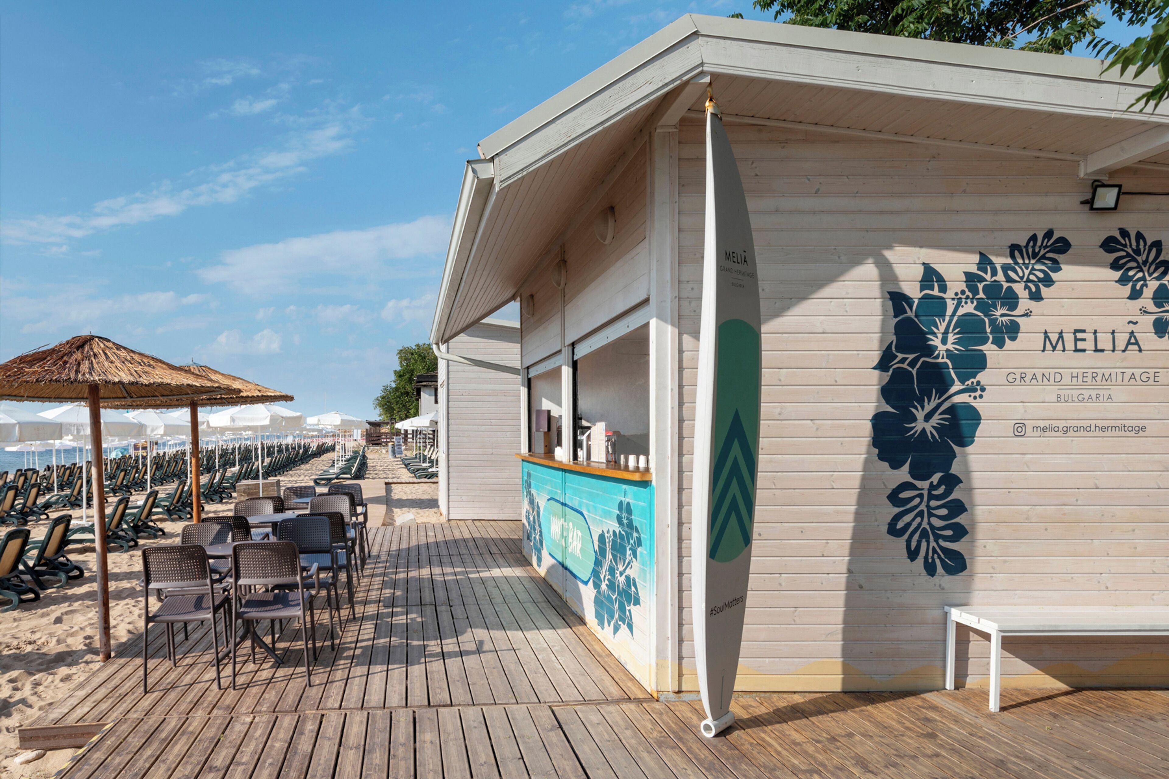 A beachside bar with a wooden deck, lounge chairs, and umbrellas.