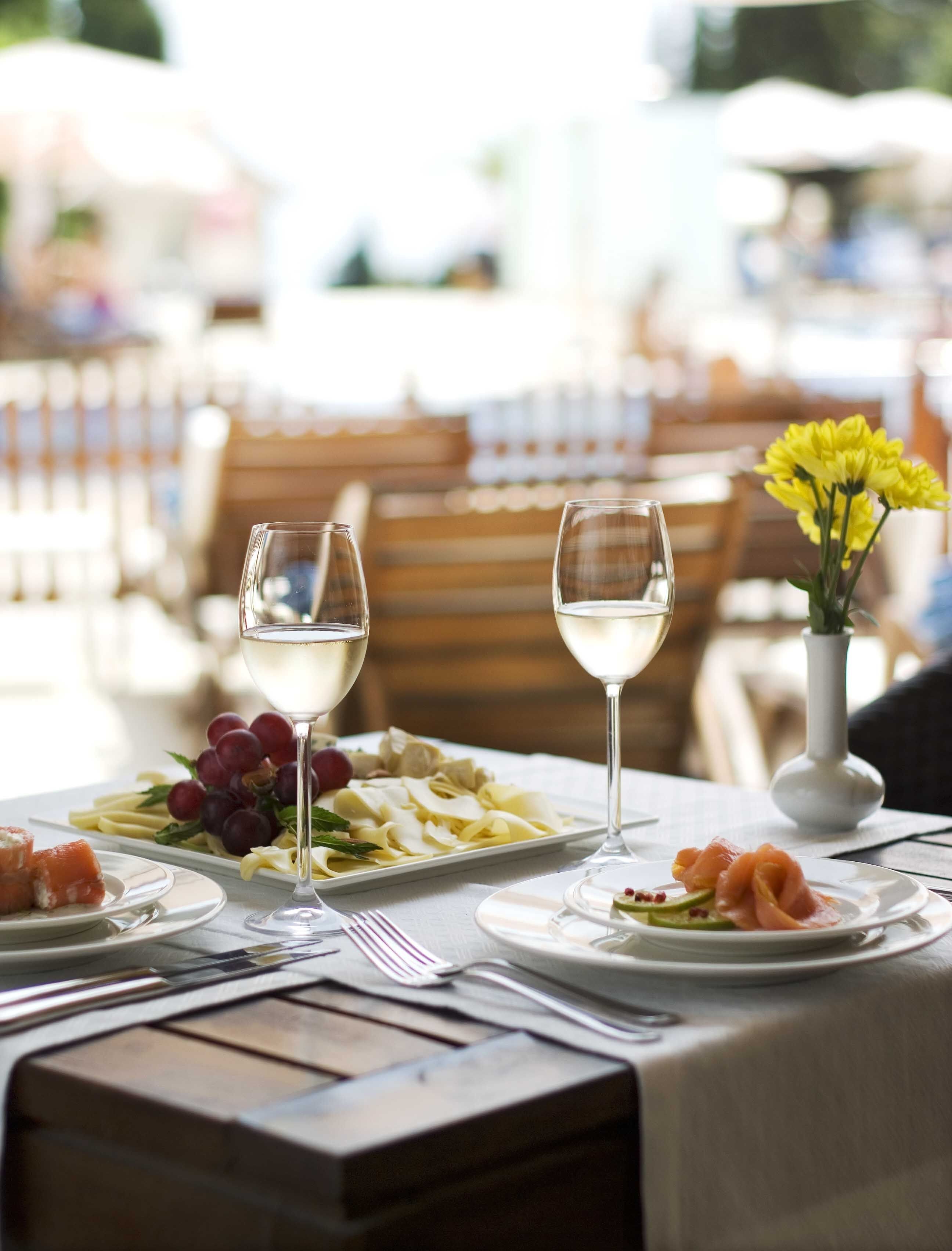 A dining table set with plates of food, two glasses of white wine, and a vase with yellow flowers.