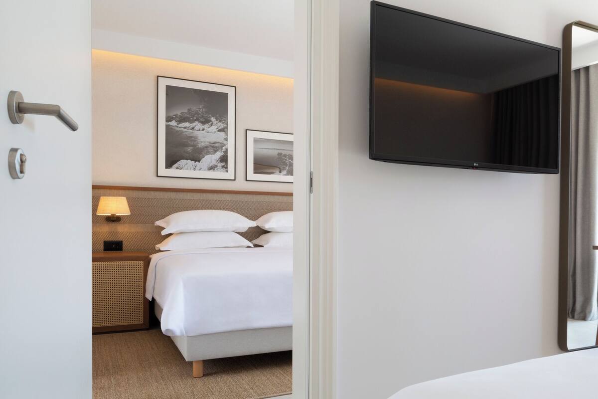 A hotel room with a bed, a flat-screen TV mounted on the wall, a bedside table with a lamp, and framed pictures on the wall.