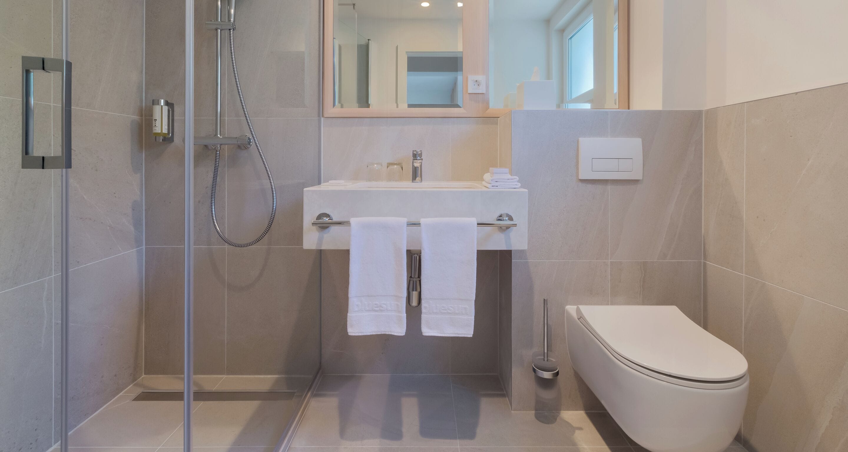 Un baño moderno con ducha de vidrio, un lavabo blanco y dos toallas, y un inodoro.