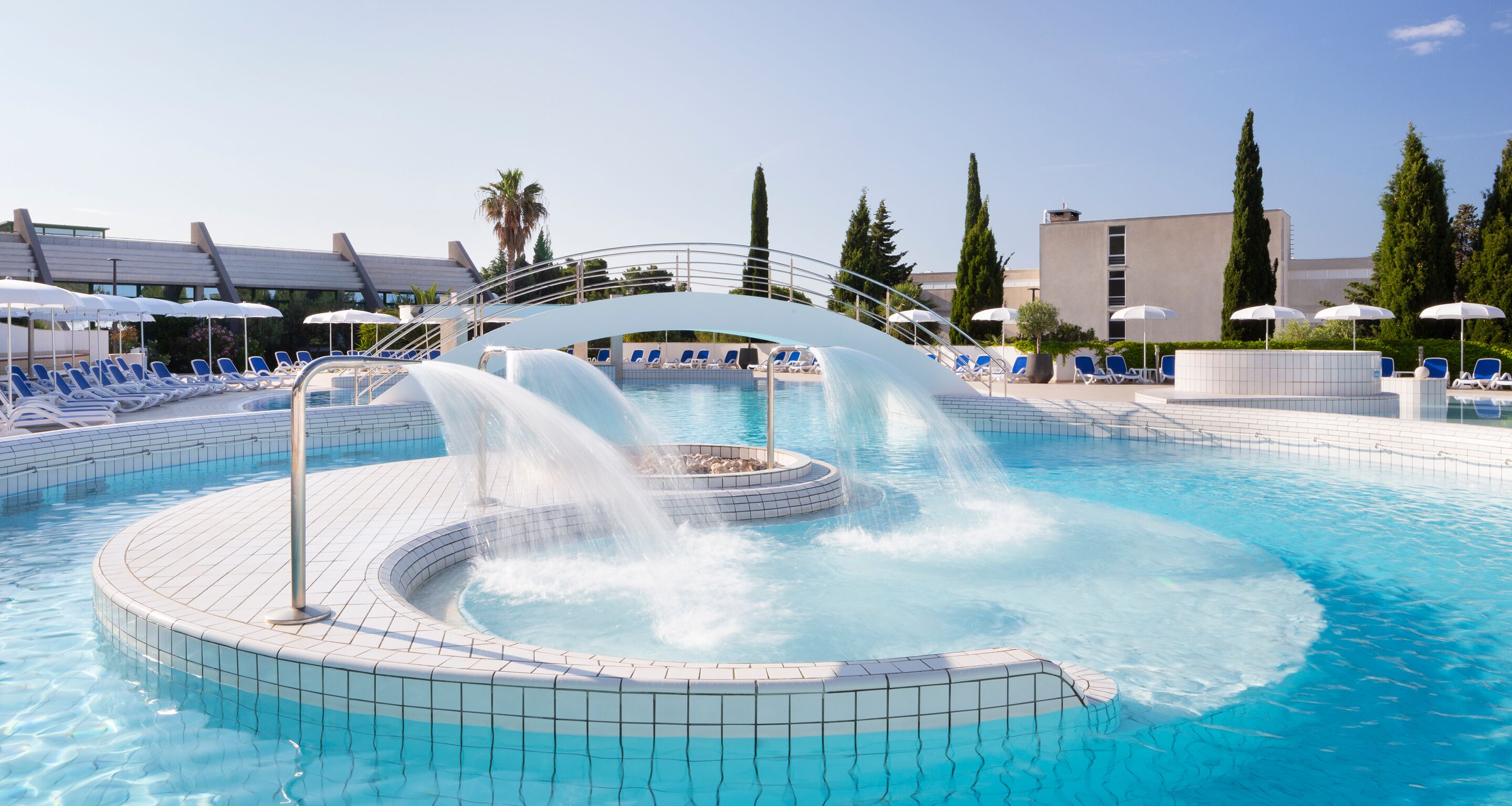 Une piscine agrémentée d’une fontaine, entourée de chaises longues et de parasols.