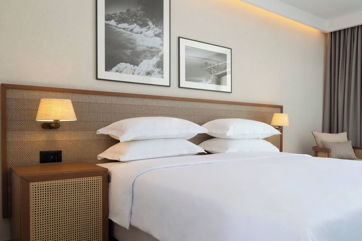 A hotel room with a large bed, two bedside tables with lamps, a headboard, and two framed pictures on the wall.