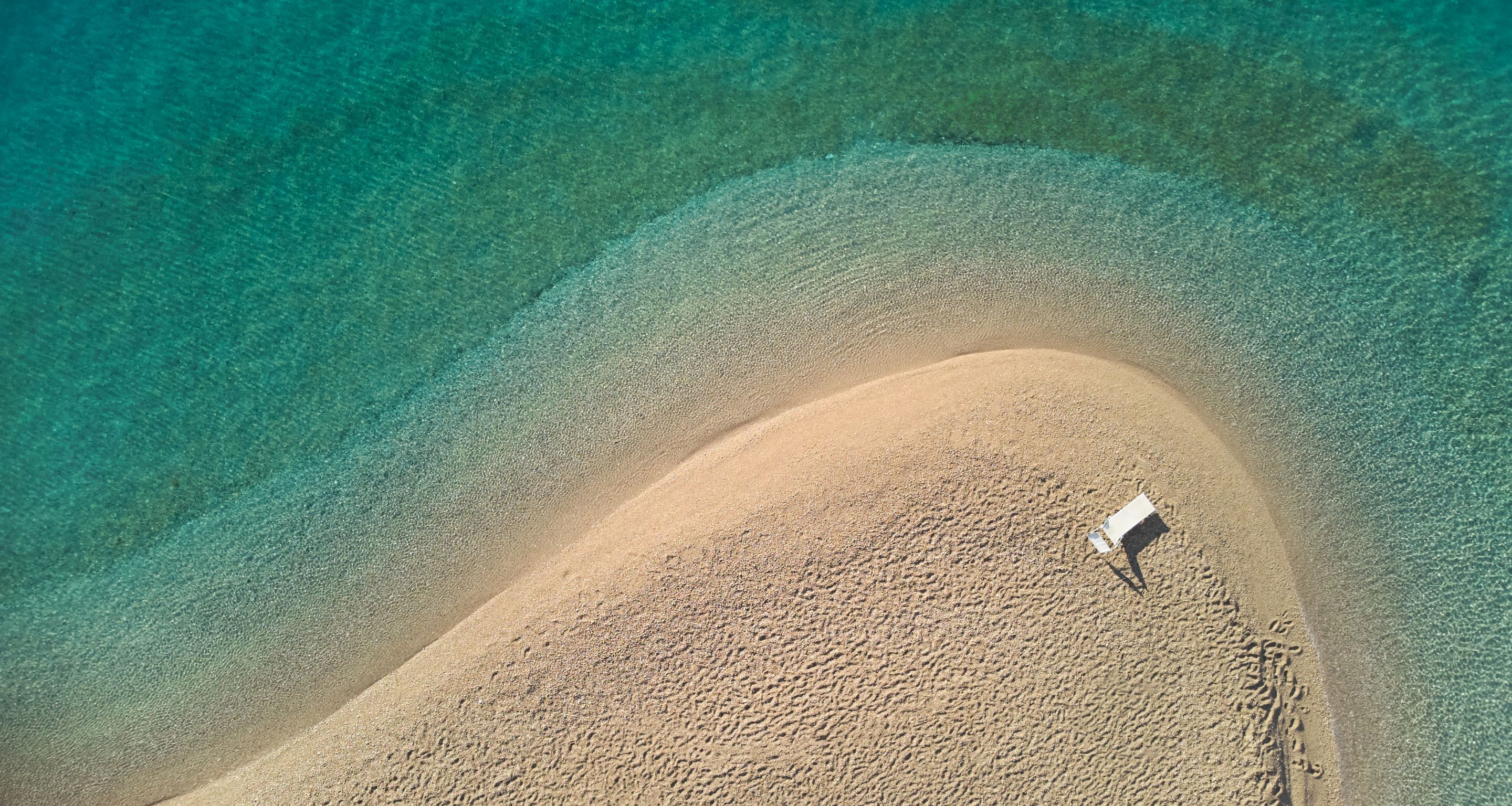 Vue aérienne d’une plage avec une seule chaise blanche sur le sable.