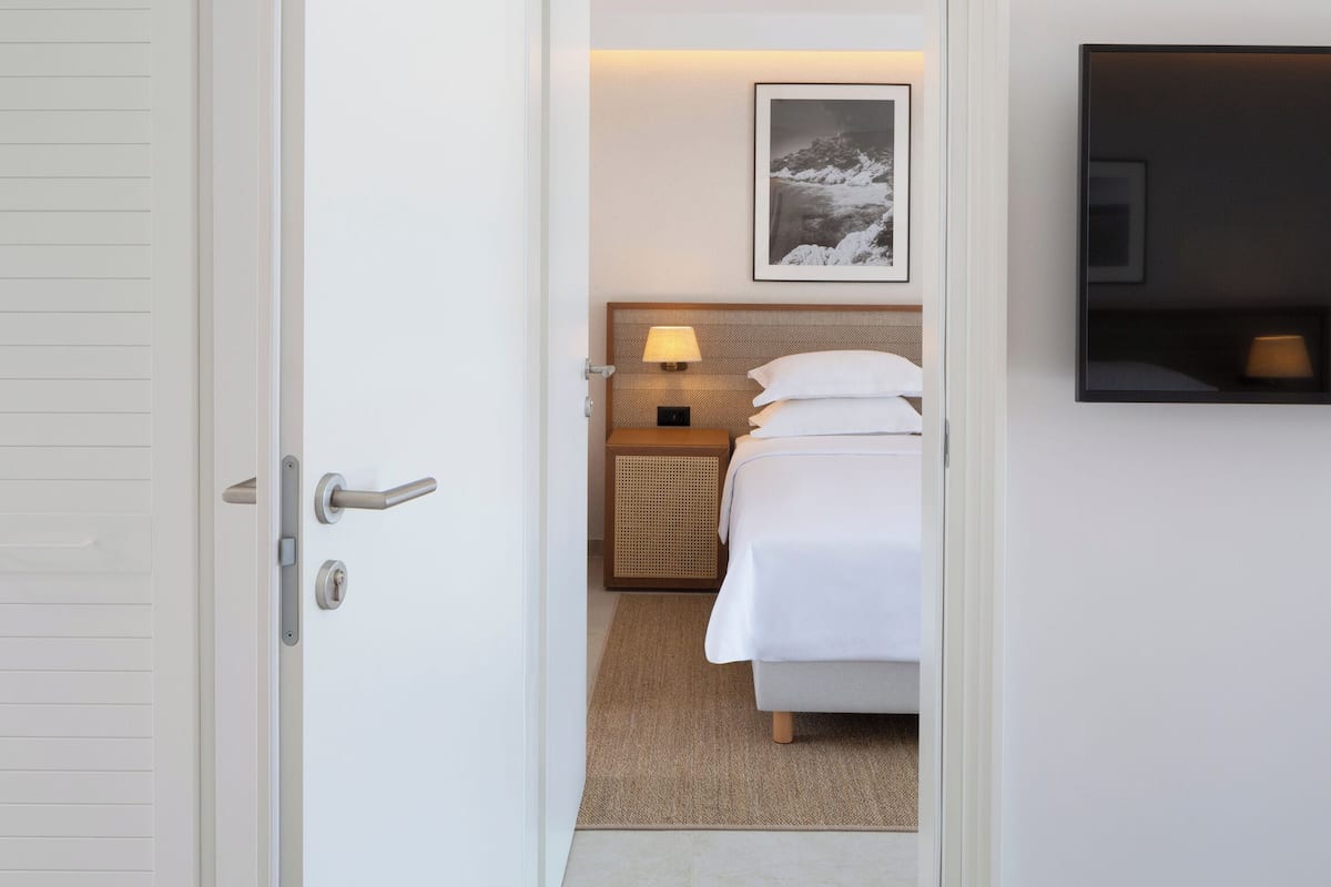 A hotel room with a bed, a nightstand with a lamp, a wall-mounted TV, and a framed picture above the bed.