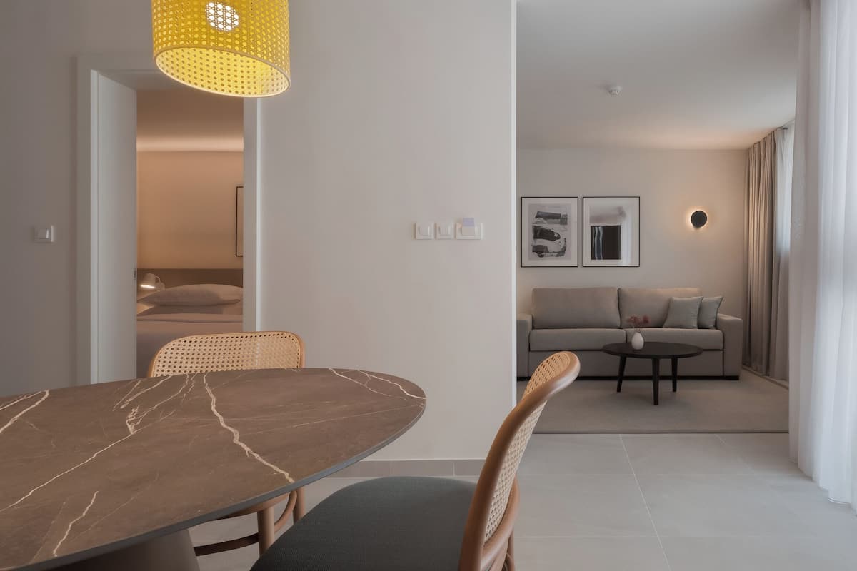 A modern living room with a sofa, a dining table with chairs, and a yellow pendant light.