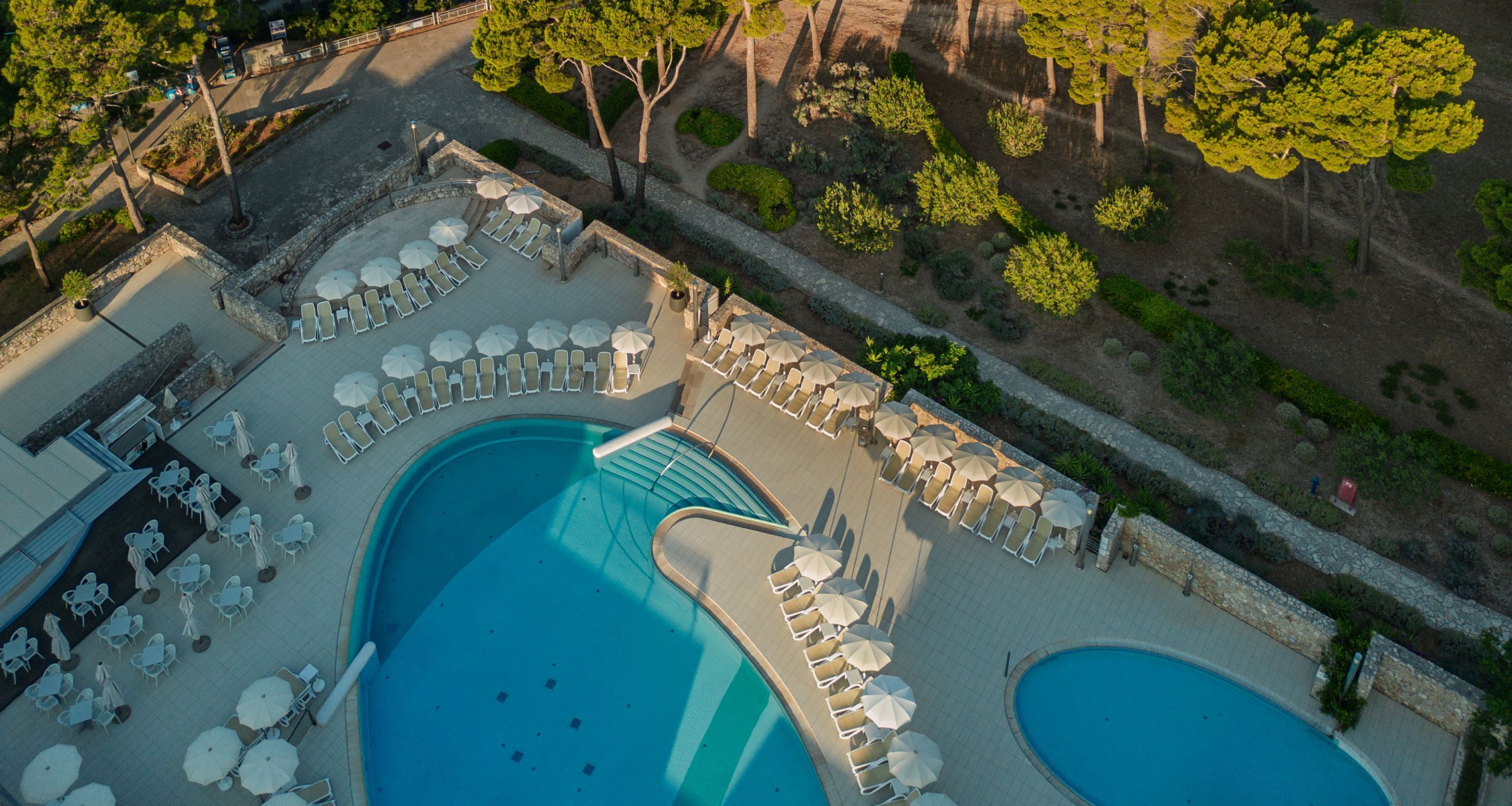An aerial view of a resort with a large pool, sun loungers, and a landscaped garden.