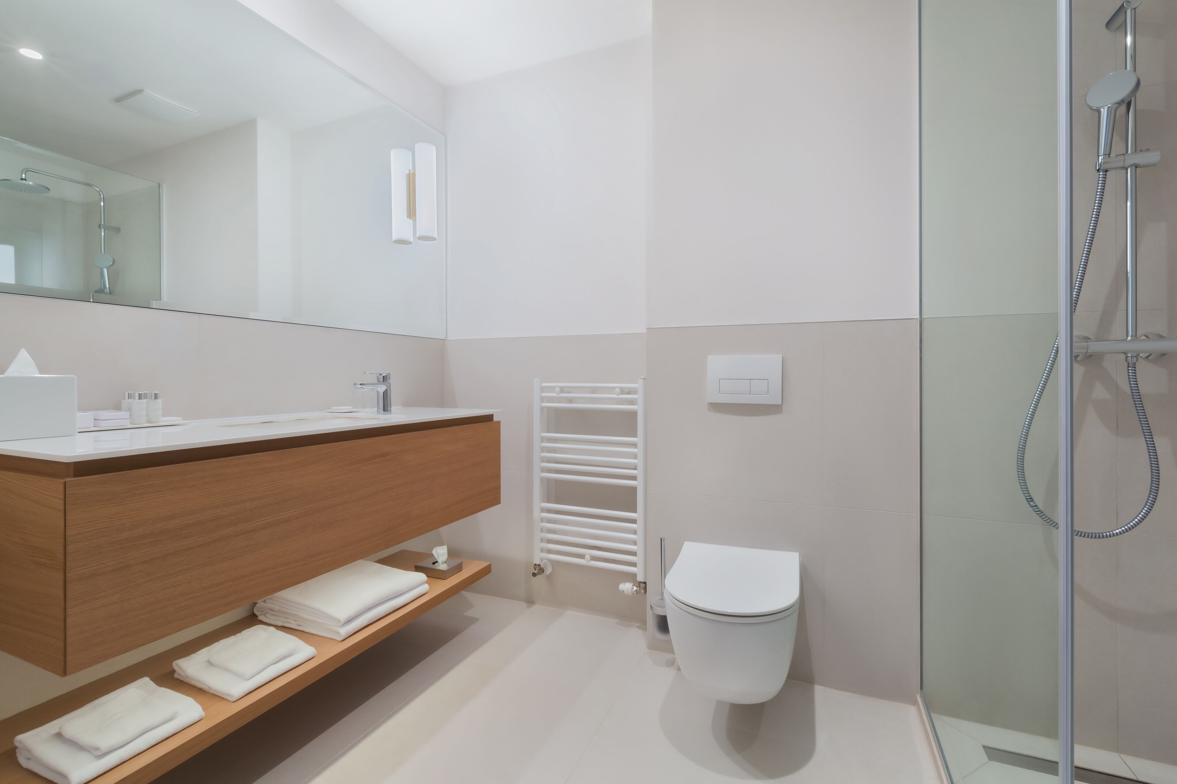 A modern bathroom with a wooden vanity, a white toilet, a glass shower enclosure, and a towel rack.