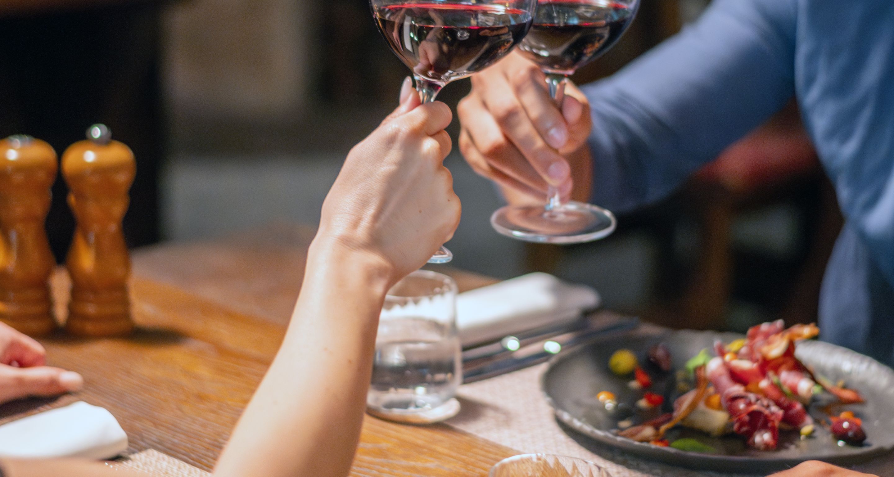 A person holding a wine glass with another person doing the same.