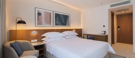 Une chambre d’hôtel avec un lit, un bureau, une chaise, une lampe et deux tableaux encadrés au mur.
