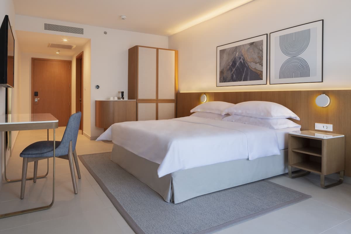 Une chambre d’hôtel moderne, dotée d’un grand lit, d’un bureau avec une chaise, d’une armoire et d’œuvres d’art accrochées aux murs.