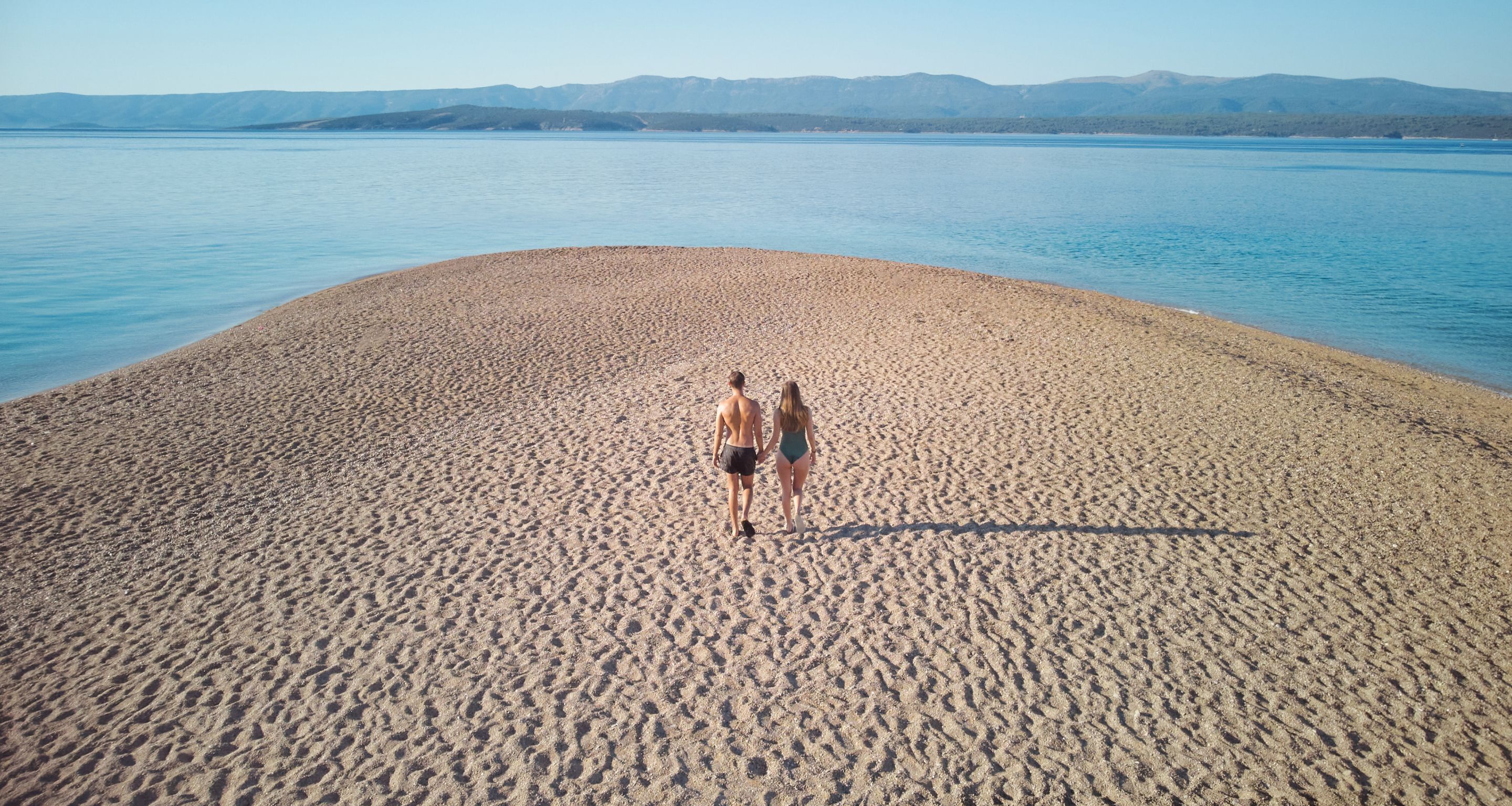 A wide, sandy beach with a calm body of water and distant mountains.