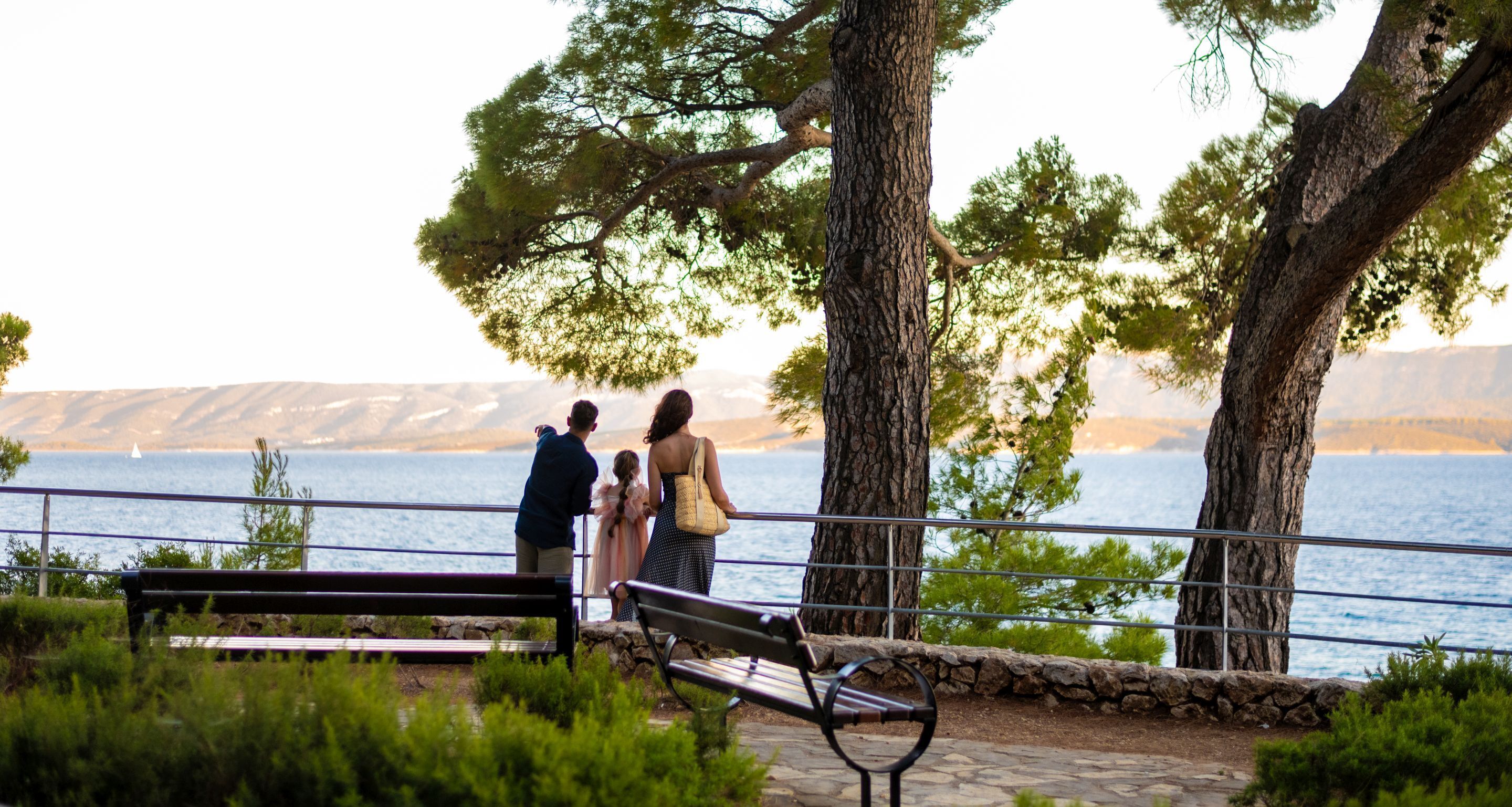 A bench and a railing overlooking a body of water with trees and mountains in the background.