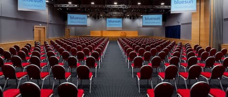 Une salle de conférence avec des rangées de chaises rouges et une scène sur laquelle est installé un grand écran affichant le logo « bluesun Hotels&Resorts ».
