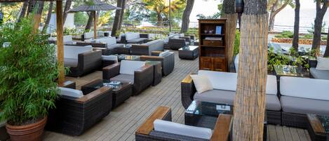 A covered outdoor seating area with wicker furniture and a wooden bookshelf.