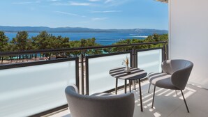 A balcony with a view of the sea and mountains, featuring two chairs and a small table with a vase.