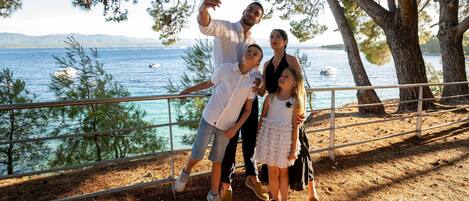 A family taking a selfie by a railing overlooking a body of water with trees and distant mountains.