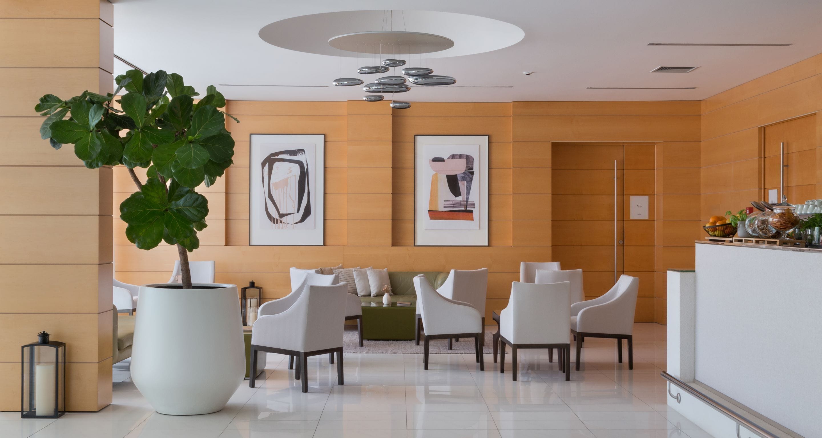 Eine moderne Lobby mit einer Rezeption, weißen Stühlen, einer großen Pflanze in einem Topf und abstrakter Kunst an den Wänden.