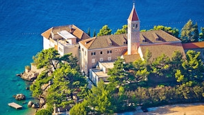 A coastal building with a prominent tower, surrounded by trees and a clear blue sea.