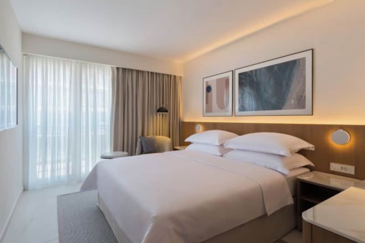 A hotel room with a large bed, a bedside table, a lamp, and a window with curtains.