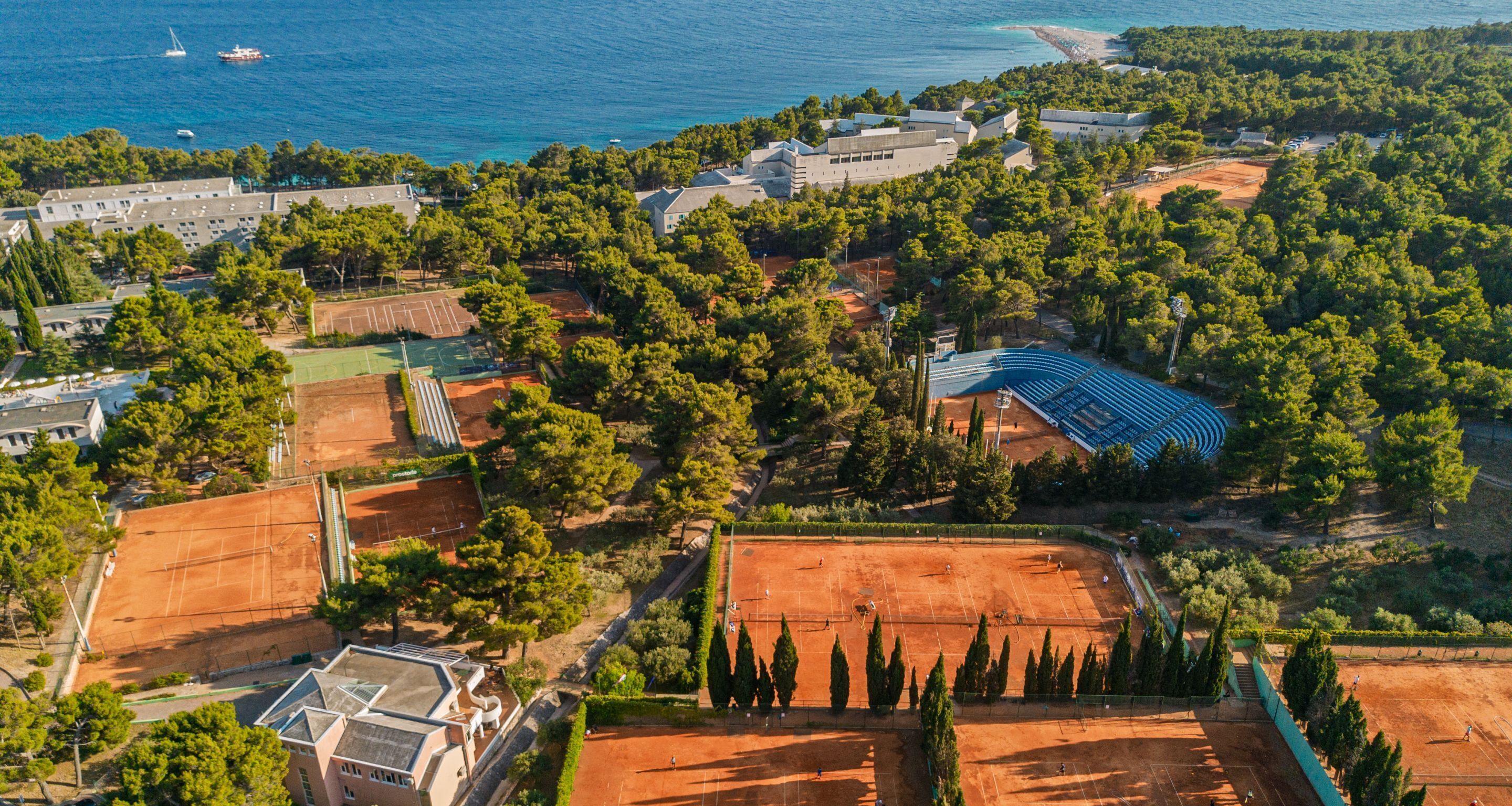 Vue aérienne d’une propriété située sur la côte, avec des courts de tennis, une piscine et une plage.
