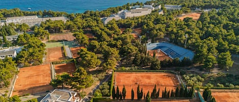 An aerial view of a coastal property with tennis courts, a swimming pool, and a beach.
