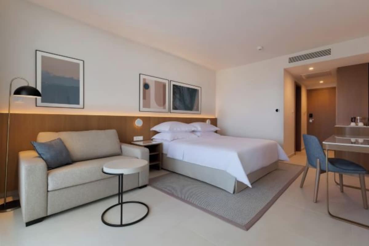 A modern hotel room with a bed, a sofa, a small table, and a desk with a chair.