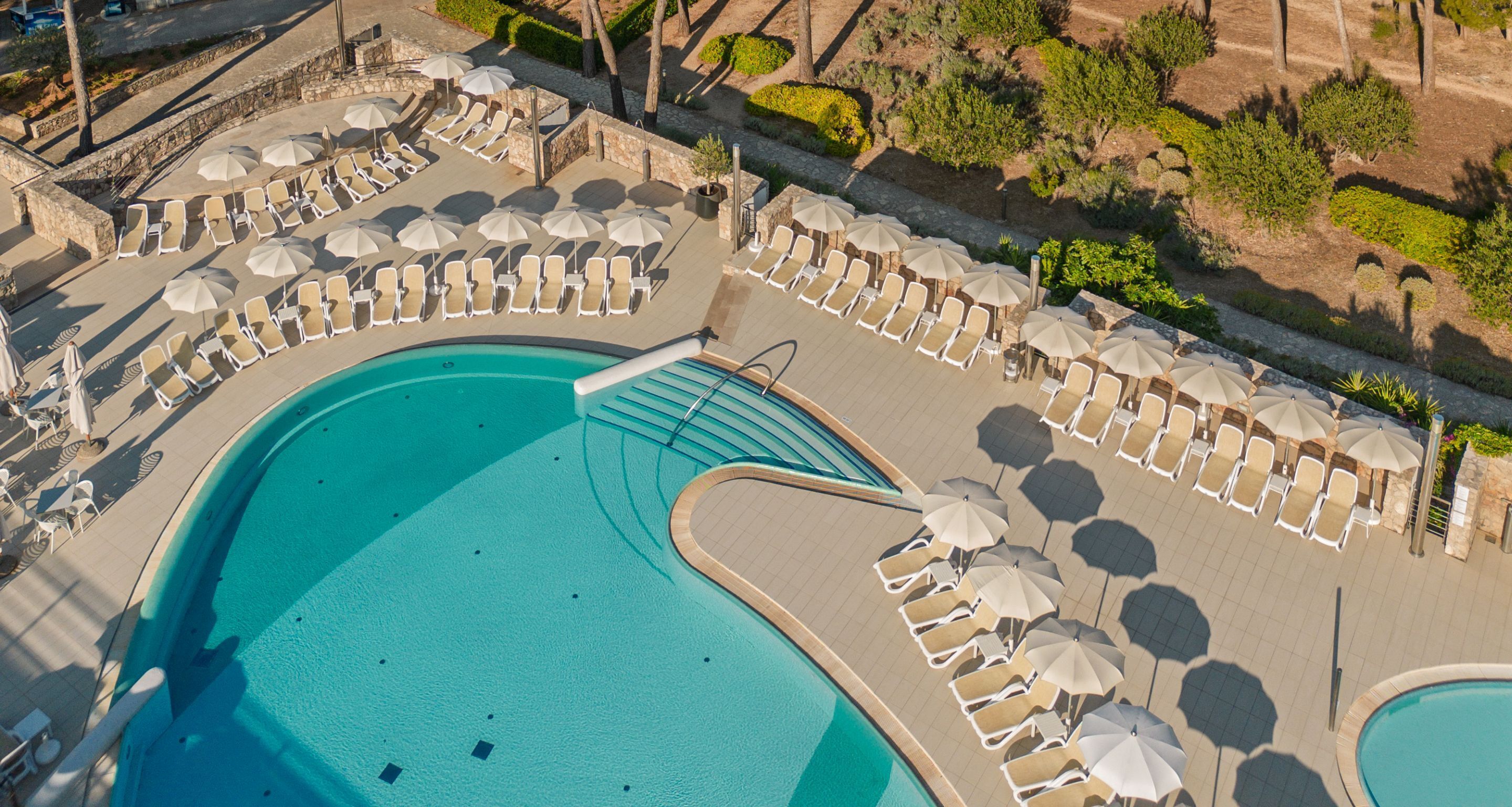 An aerial view of a resort pool area with sun loungers and umbrellas arranged around a central pool.