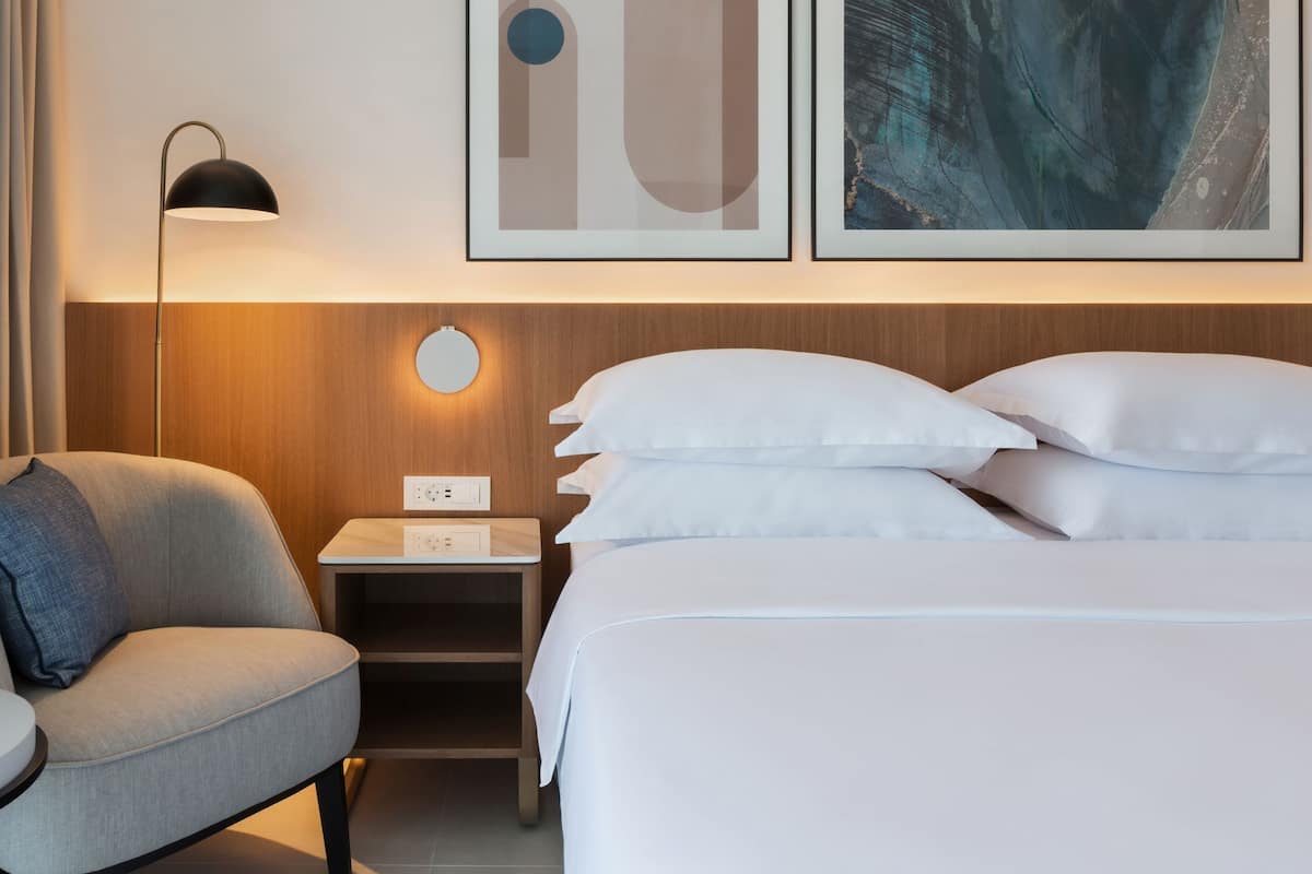Une chambre d’hôtel avec un lit, une chaise, une table de chevet, une lampe et des œuvres d’art au mur.