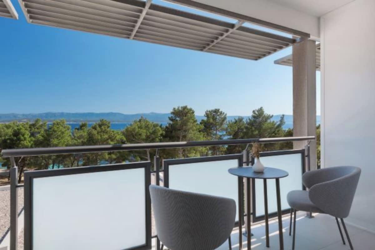 A balcony with a view of the sea and mountains, two chairs, and a small table.