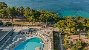 A resort with a swimming pool, sun loungers, umbrellas, and a view of the sea.