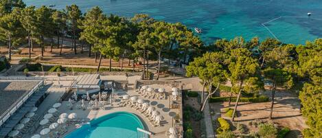 Un resort con piscina, tumbonas, sombrillas y vista al mar.