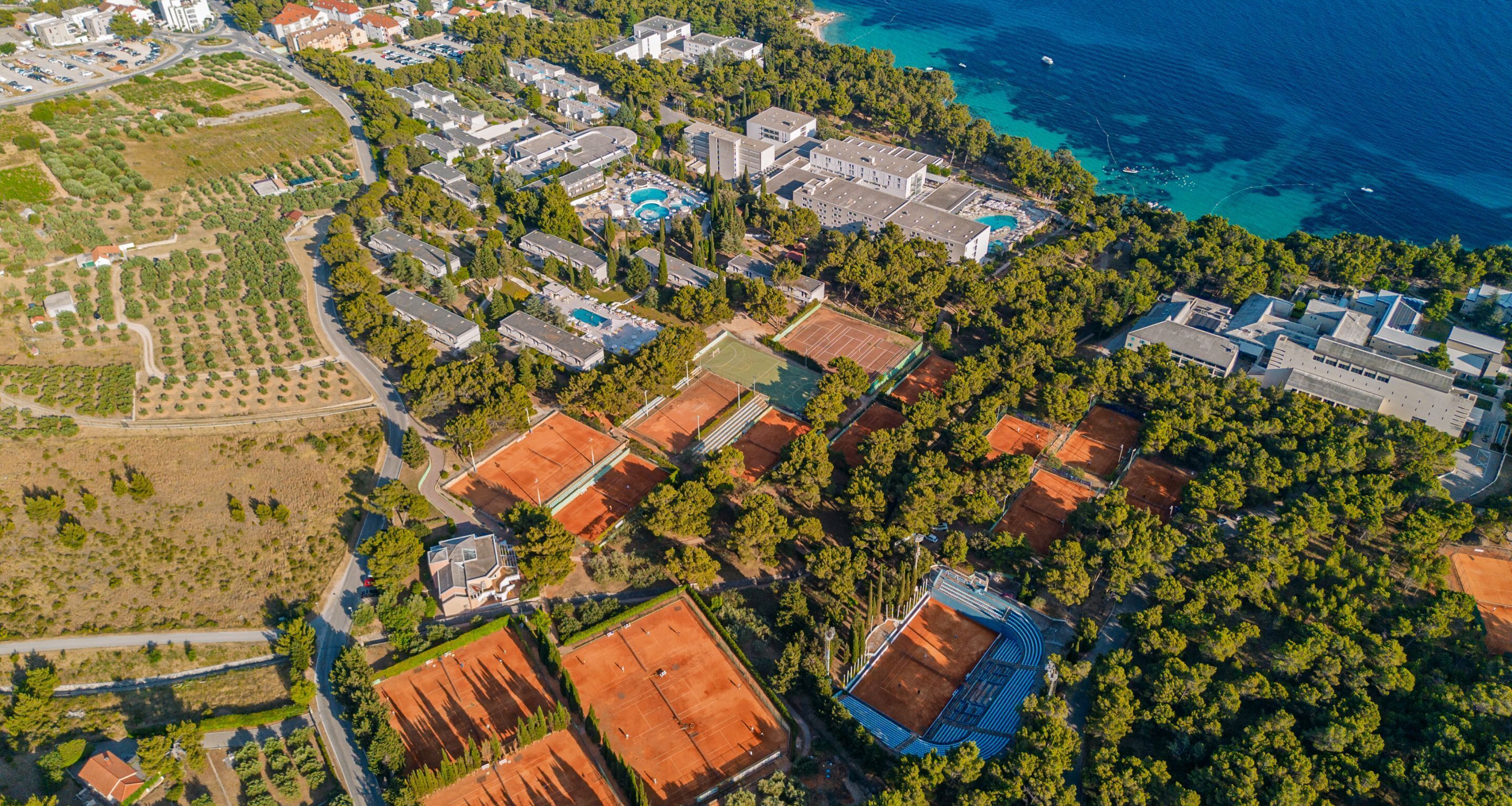 An aerial view of a residential area with multiple buildings, a tennis court, and a swimming pool.