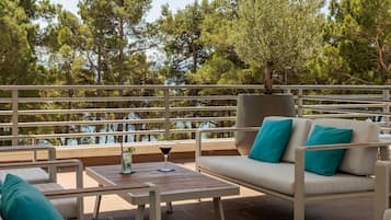 Ein Balkon mit einer Couch und Stühlen, ein Tisch mit Getränken und Blick auf Bäume und Wasser.