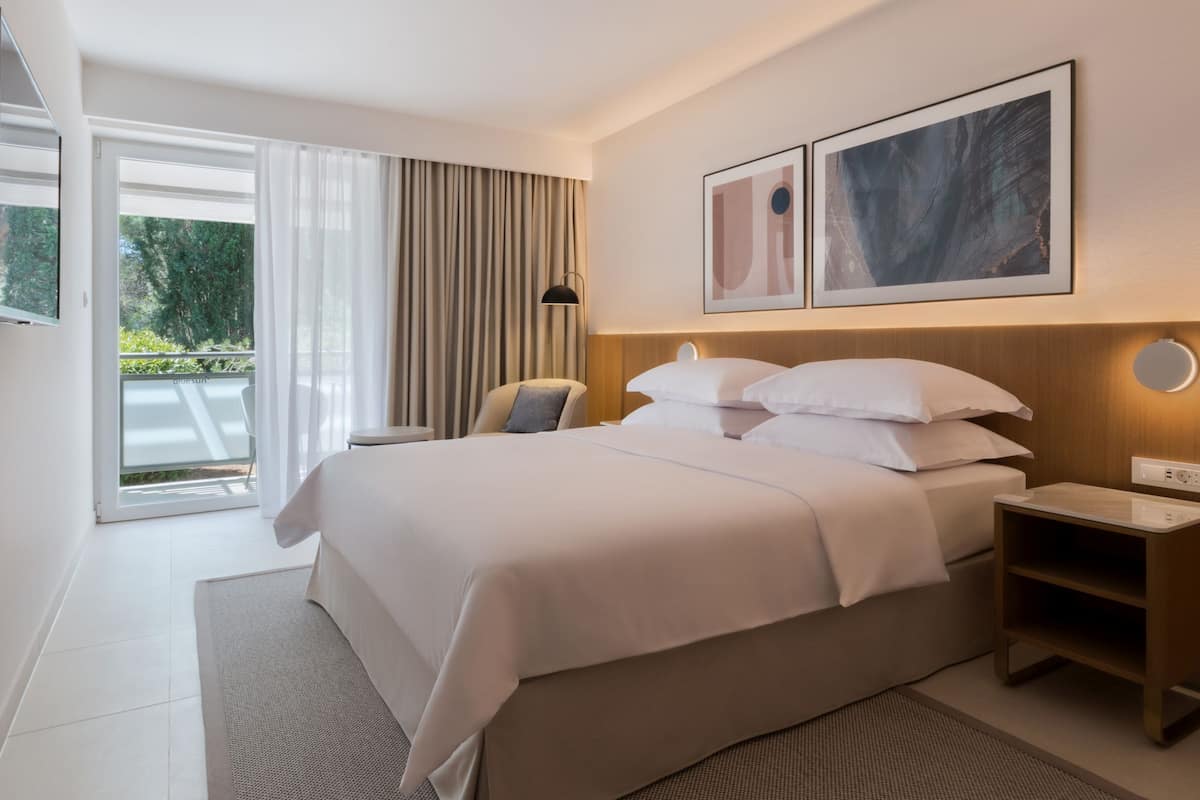 Une chambre d’hôtel moderne avec un grand lit, une table de chevet, un téléviseur fixé au mur et une fenêtre avec des rideaux.