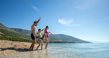 Una playa con agua cristalina, costa rocosa y montañas al fondo.
