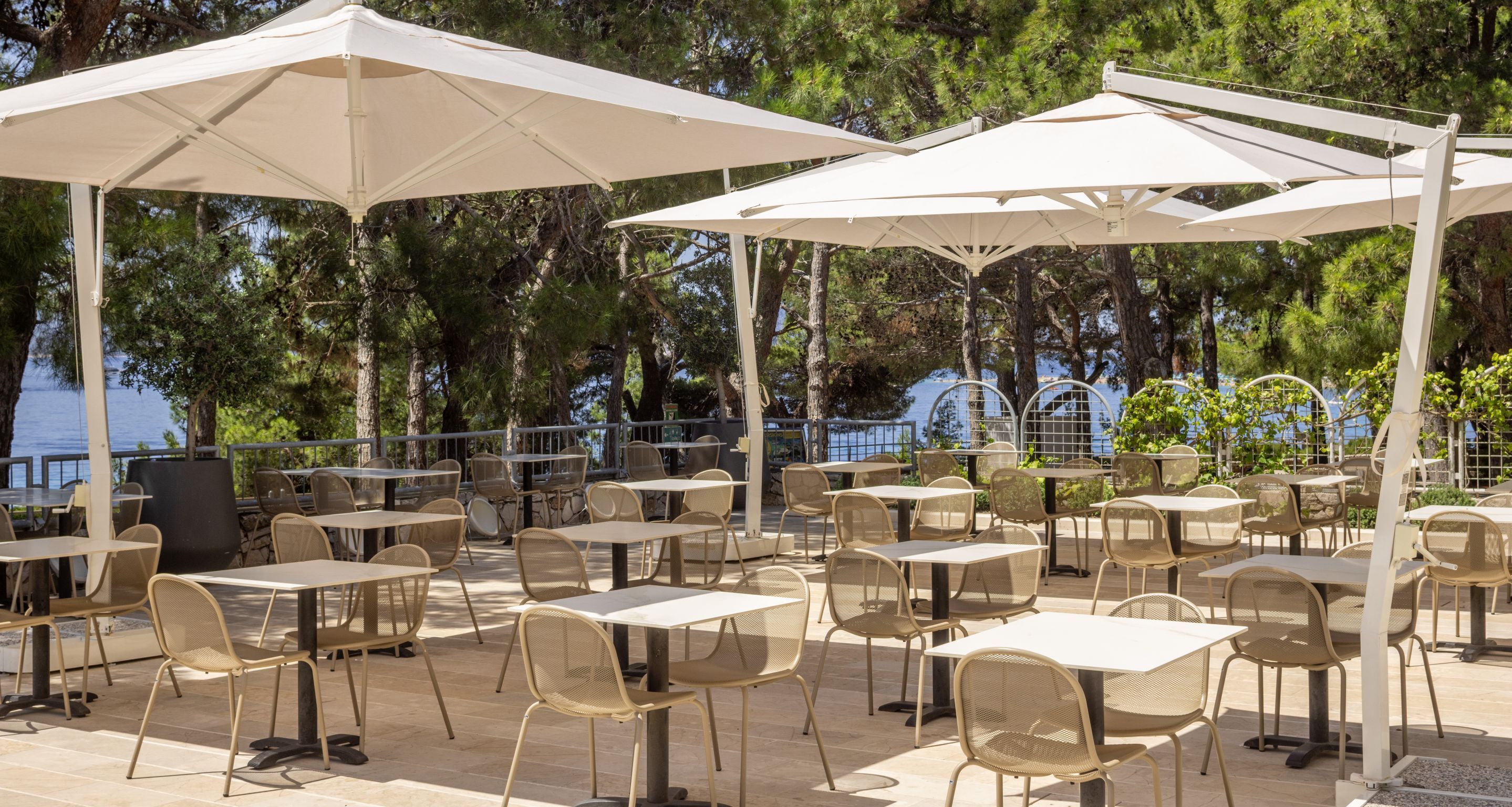 An outdoor patio with tables and chairs under white umbrellas, overlooking a body of water.