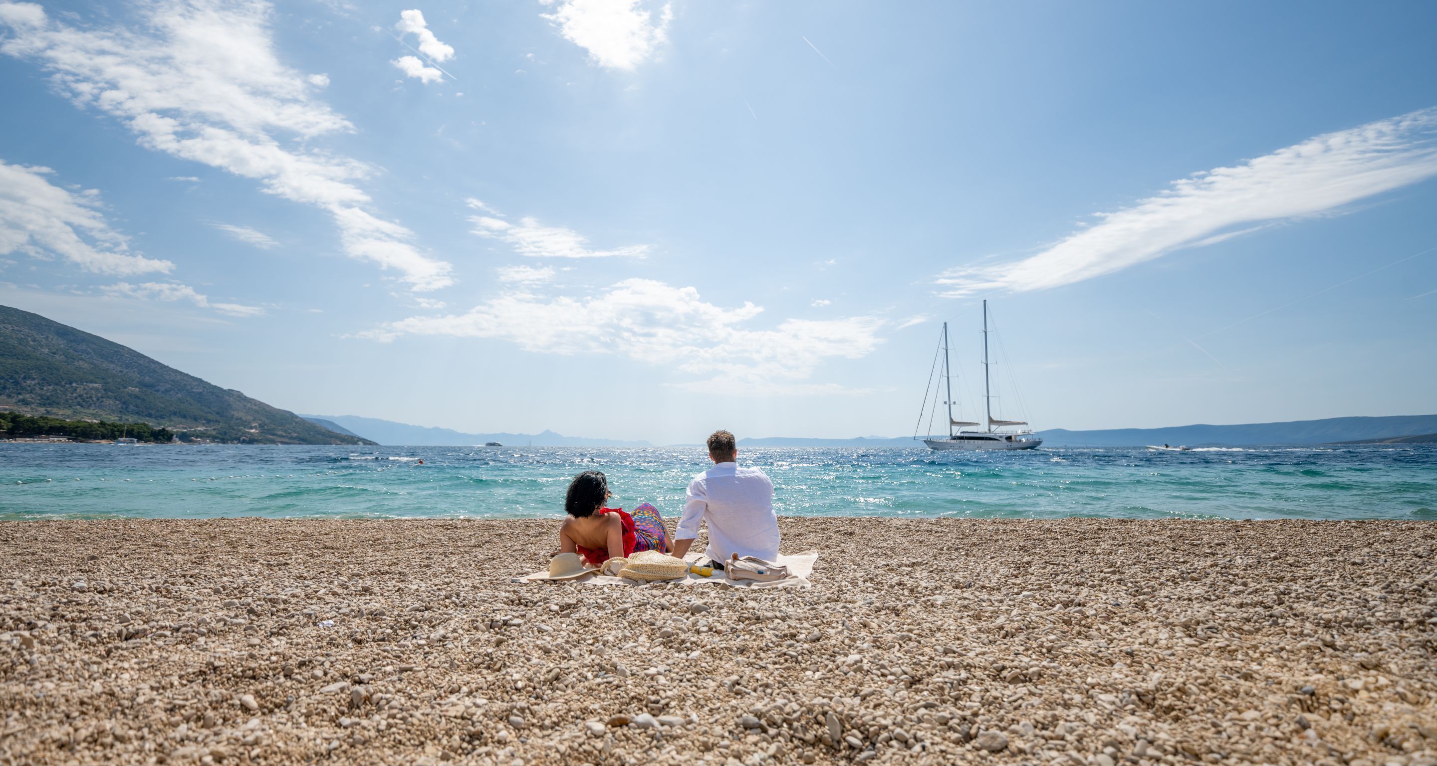 Ein Kiesstrand mit einem Segelboot in der Ferne.