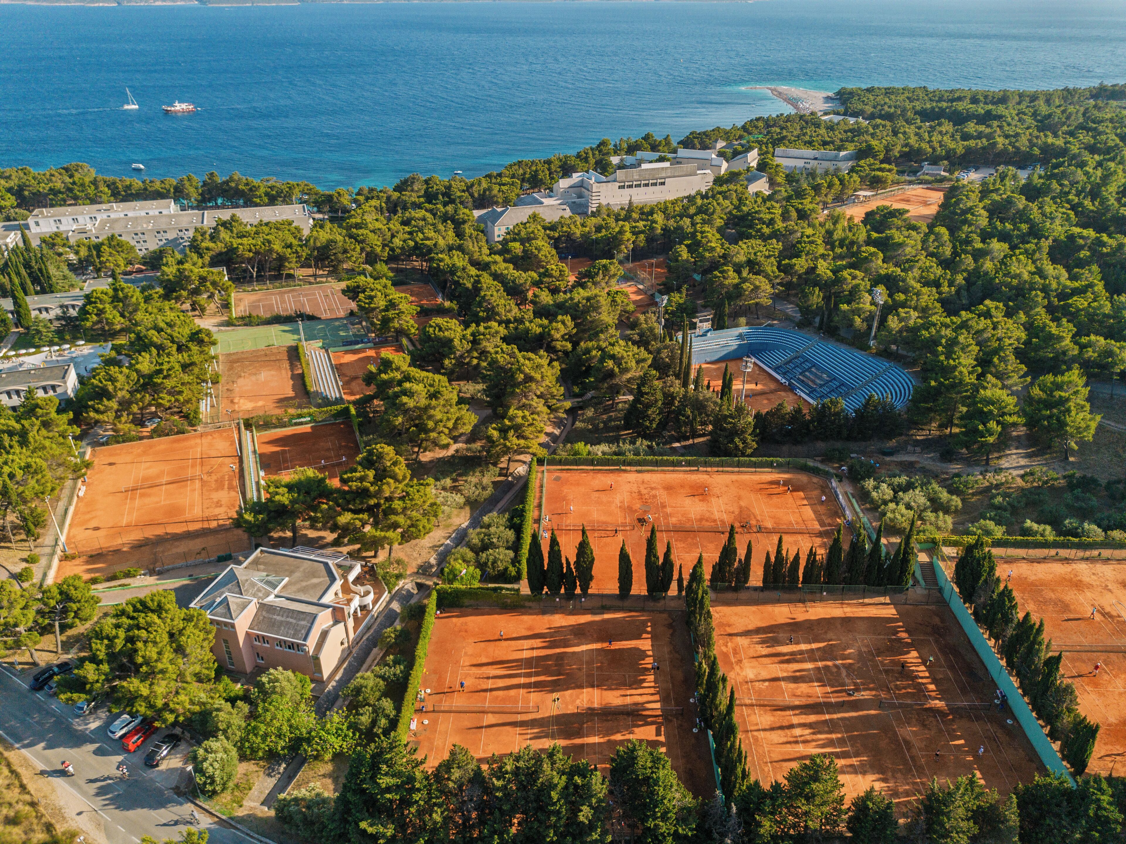 Vista aérea de una propiedad costera con canchas de tenis, piscina y playa.