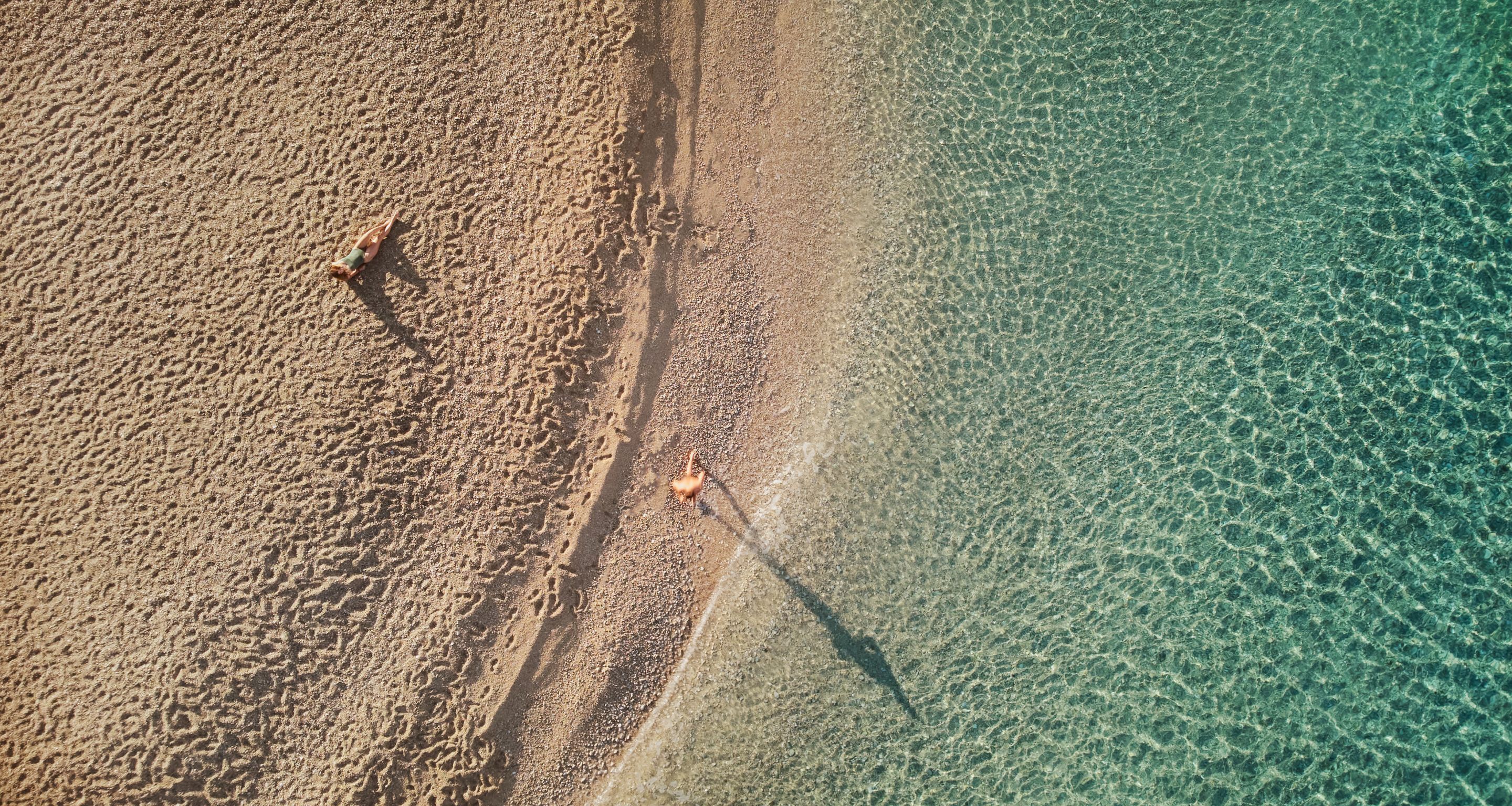 En vy över en strand sedd från luften, med klart vatten och sand.